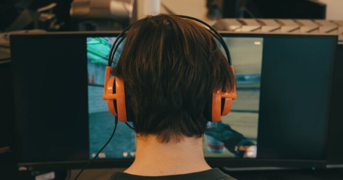 Guy with headphones sitting in front a computer screen playing game