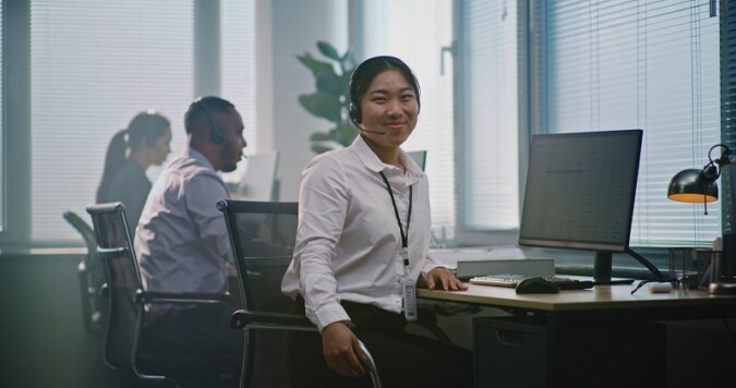 A smiling customer service representative wearing a headset in a modern call center