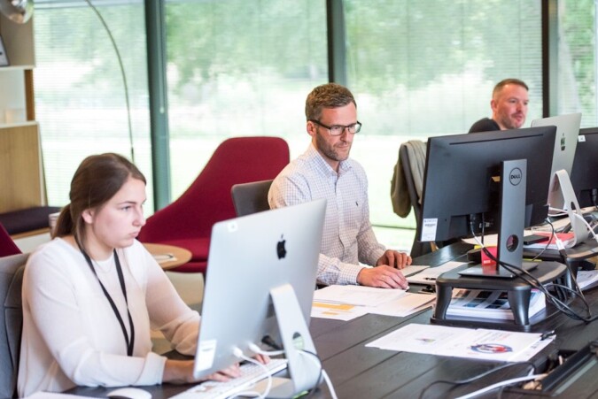 Team members collaborating in an office setting, seated at their table with computers in front of them, improving efficiency and productivity through fax automation