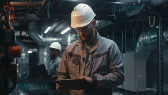 An engineer in a hard hat reviews technical data on a tablet inside an industrial facility