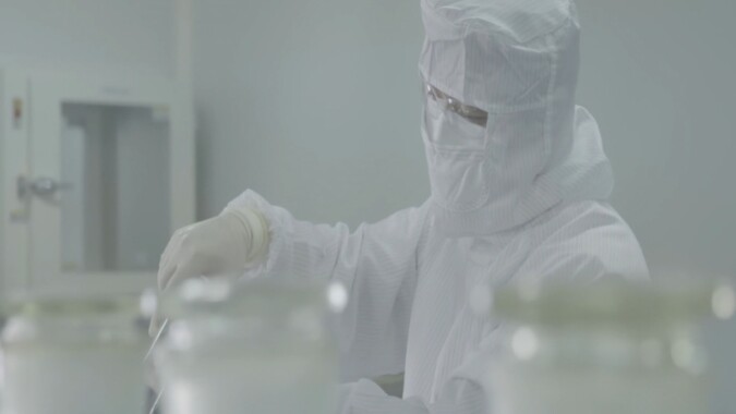 An engineer in cleanroom gear performs careful testing in a controlled lab environment