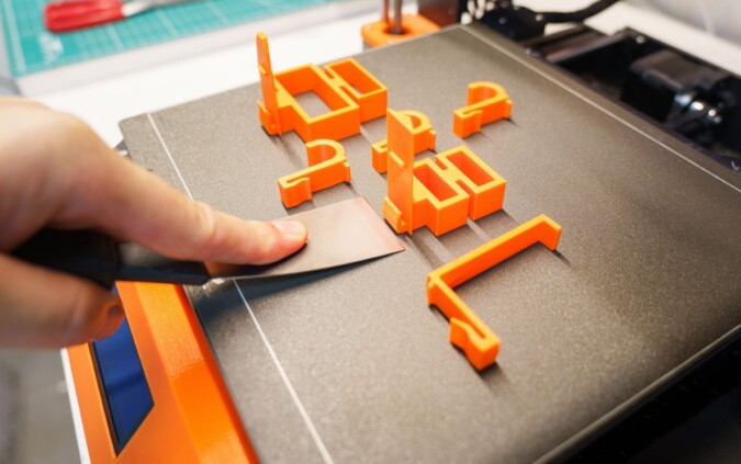 Hand removing a freshly 3D-printed prototype from a printer bed